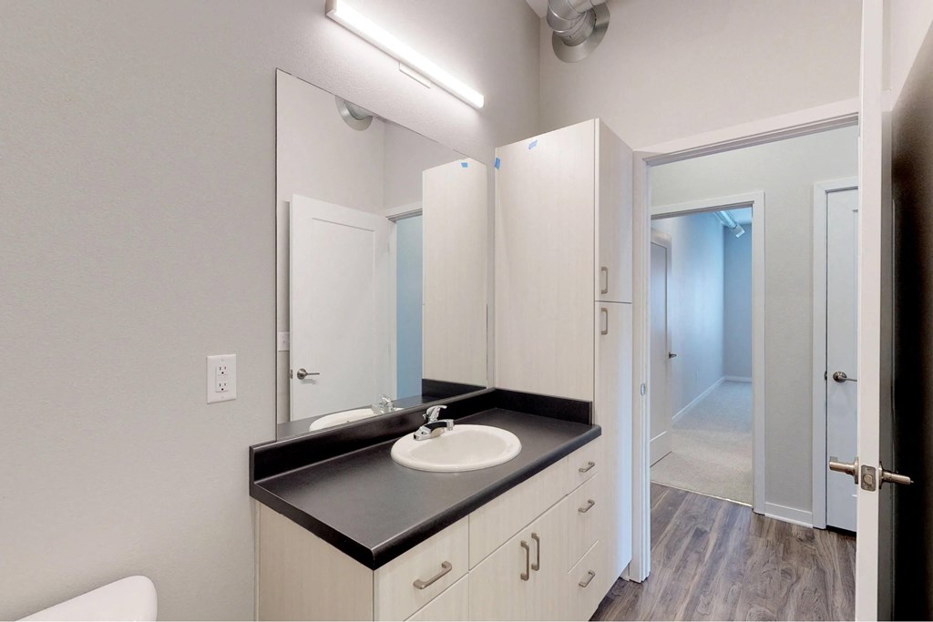 a white bathroom with a black counter top and a mirror at Vue Apartments, Des Moines, IA 50309