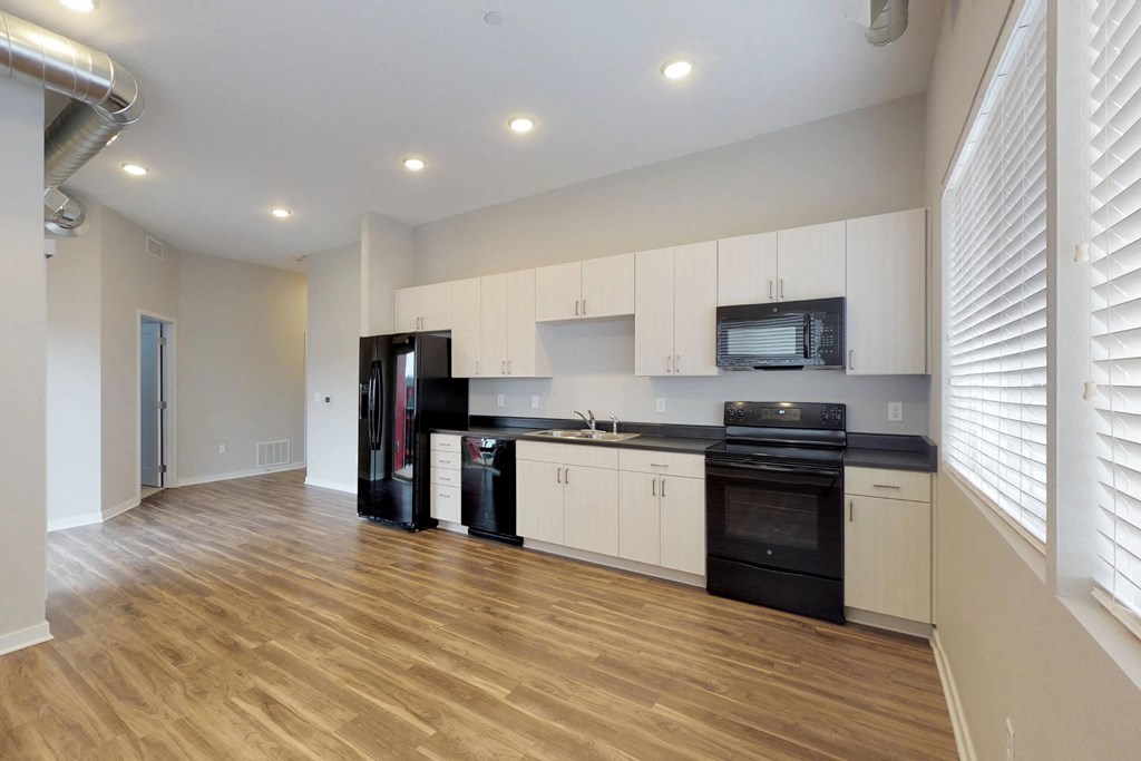 a kitchen with white cabinets and black appliances and a wooden floor at Vue Apartments, Des Moines