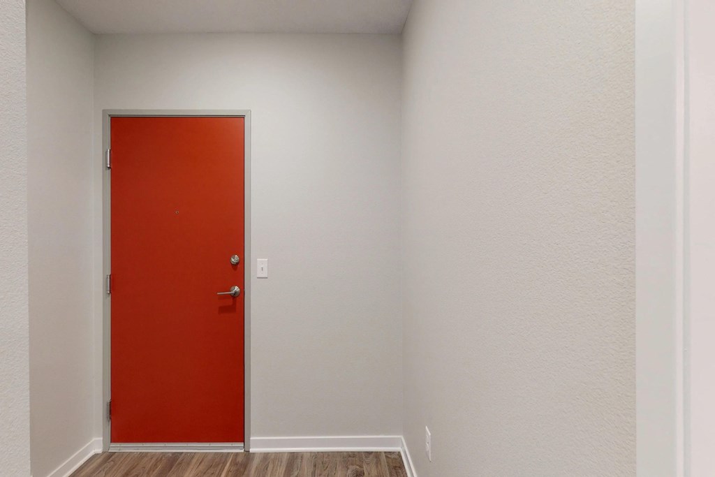 a red door in an empty room with white walls and wood floors at Vue Apartments, IA, 50309