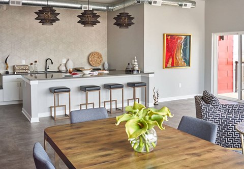 A kitchen with a bar and a dining table with a vase of flowers on it.