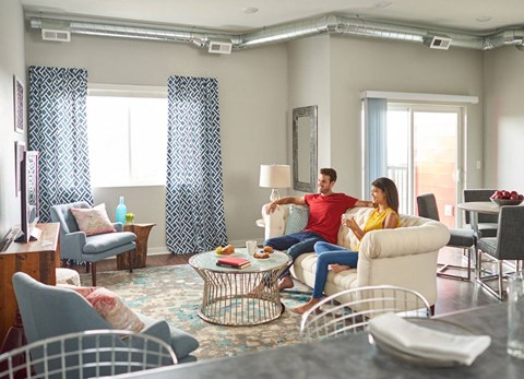 A man and woman are sitting on a couch in a living room with a coffee table in front of them.