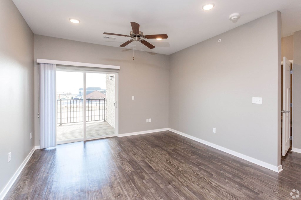 an empty living room with a ceiling fan and a sliding glass door at The Barclay Apartments, IOWA