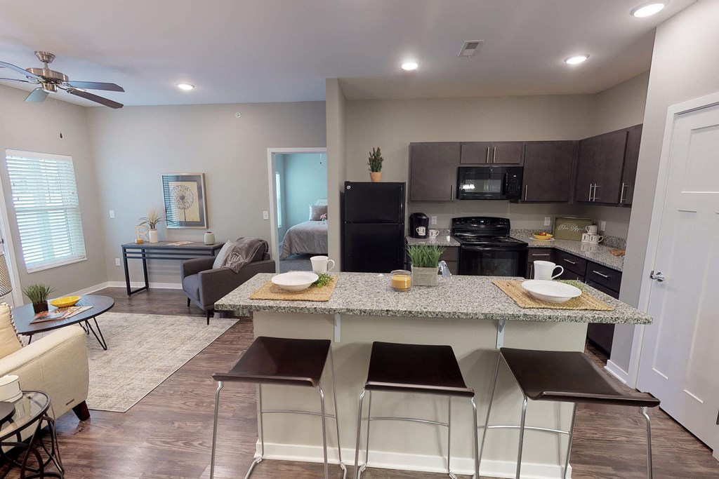 A kitchen with a black fridge and microwave, a dining table with chairs, and a living room with a couch and a coffee table. at The Barclay Apartments, IOWA, 50009