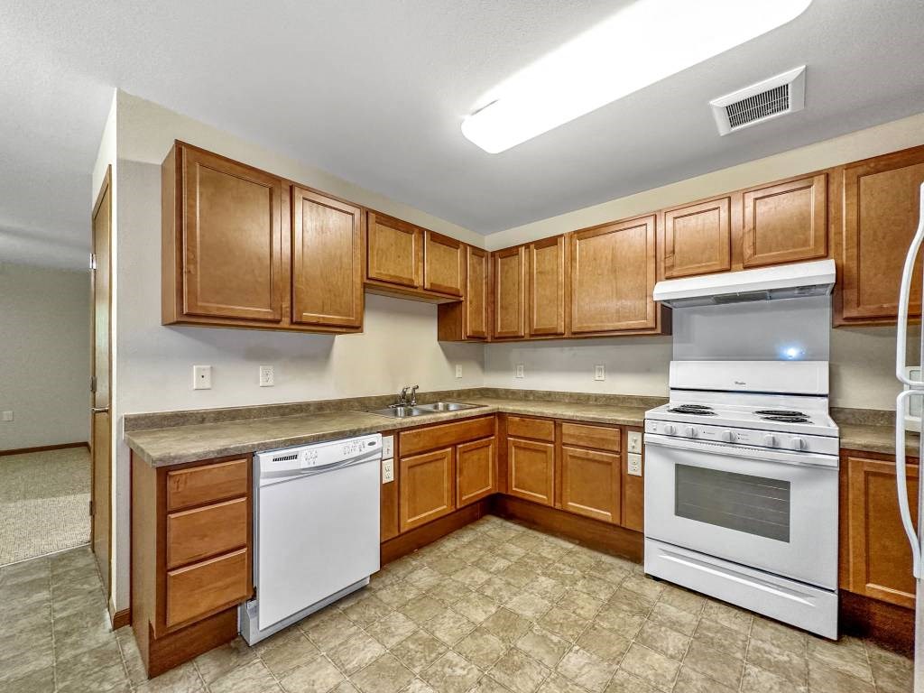 A kitchen with white appliances and wooden cabinets.at Cornerstone Commons, Iowa, 50131