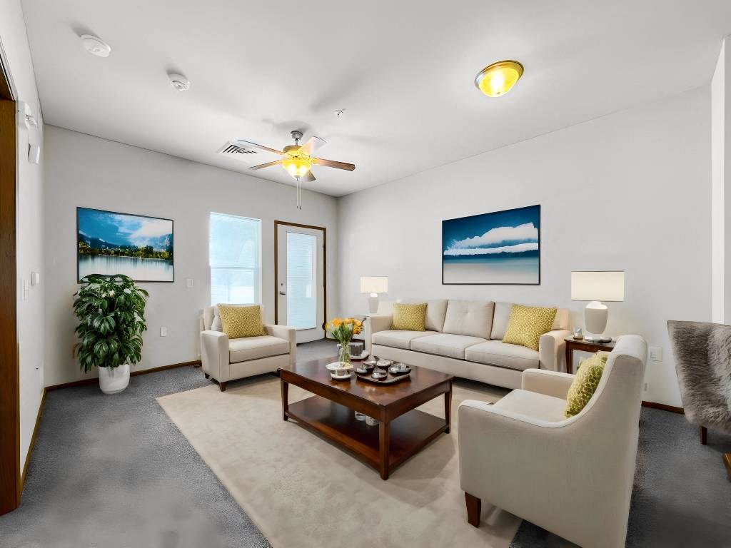 A living room with a white couch, a coffee table, and a ceiling fan.at Cornerstone Commons, Johnston, IA  