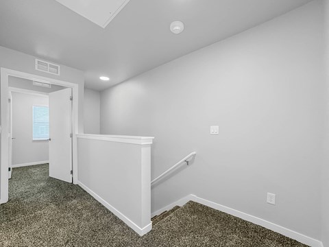 A room with a carpeted floor and a staircase leading to another room.at Hawthorne Pointe, Iowa, 50035