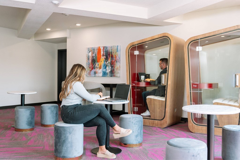 A woman is sitting on a stool in a room with a wooden pod-like structure.at Level, Des Moines, 50309  