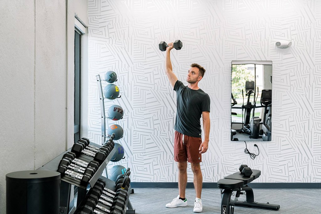 A man lifting dumbbells in a gym with a mirror and weight rack.at Level, Iowa   
