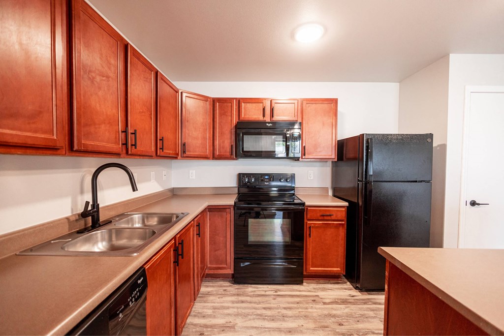 A kitchen with wooden cabinets and black appliances at Meadowlark Place Apartments, Grimes, IA,  50111