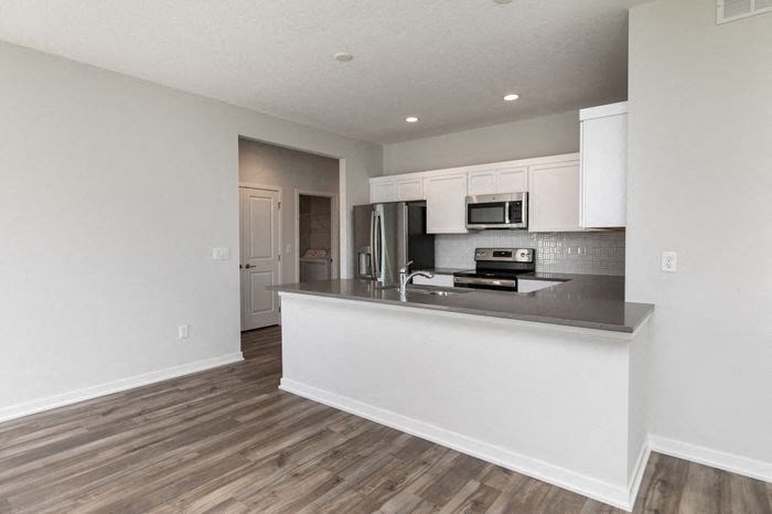 A kitchen with white cabinets and a wooden floor. at Two Rivers Home Rentals, Iowa 50266