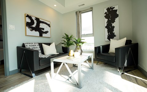 A living room with a black couch, a white coffee table, and a large abstract painting on the wall.