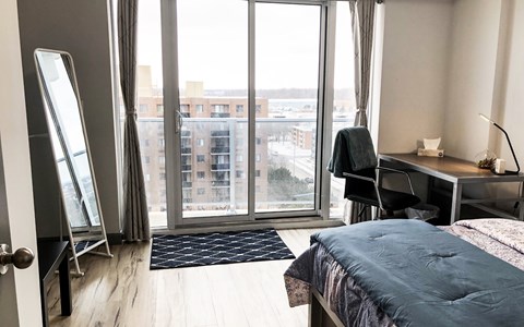 A bedroom with a large bed, desk, and a view of the city through the window.