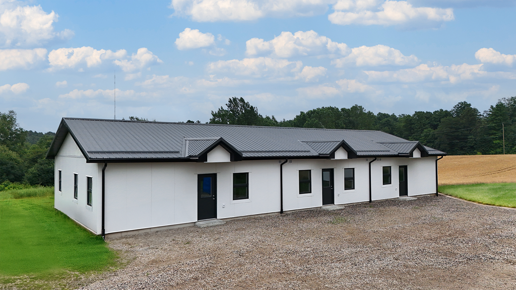 A white house with a black roof is surrounded by a gravel driveway.