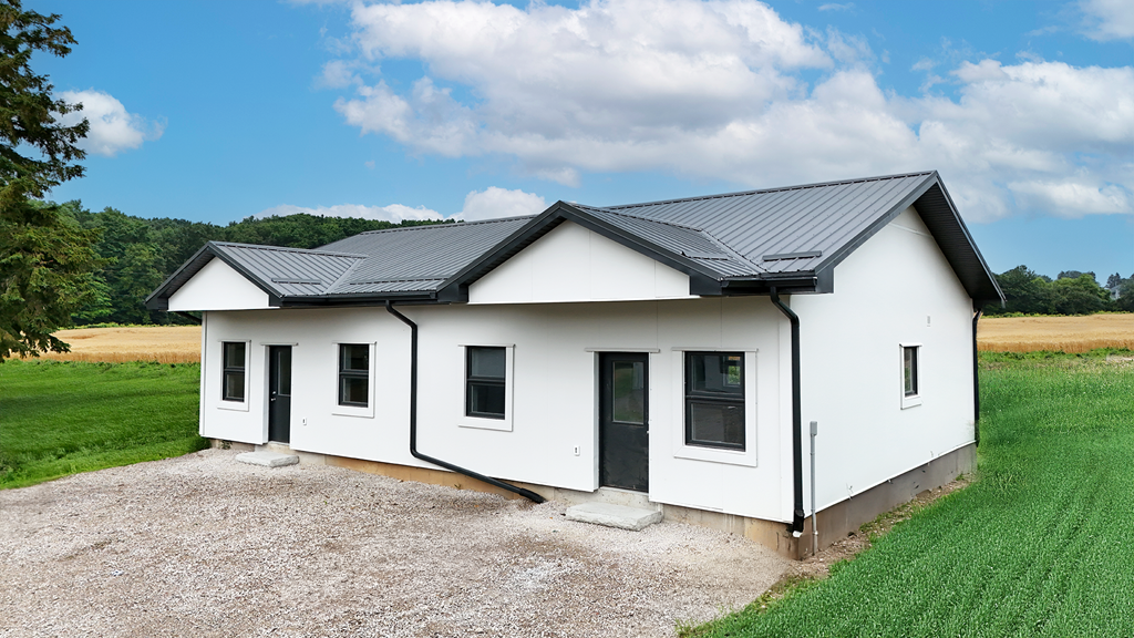 A white house with a black roof is surrounded by a gravel driveway.