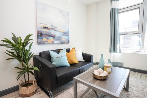 A living room with a black couch, a wooden coffee table, and a large painting on the wall.