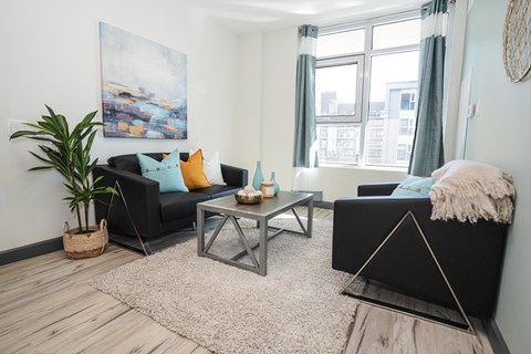 A living room with a black couch, a coffee table, and a large painting on the wall.