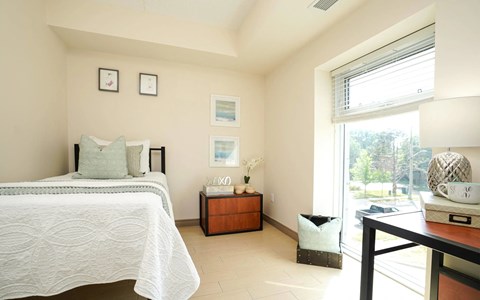 A bedroom with a bed, nightstand, and a table with a lamp.