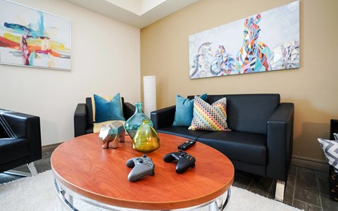 A living room with a black couch, a wooden table, and two Xbox controllers on it.