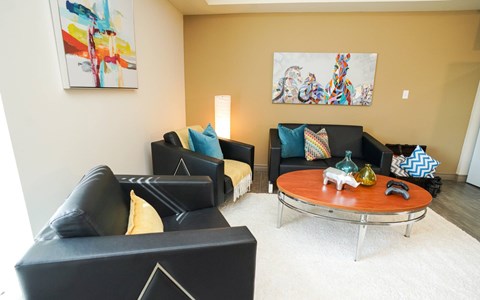 A living room with a black couch, a coffee table, and two paintings on the wall.