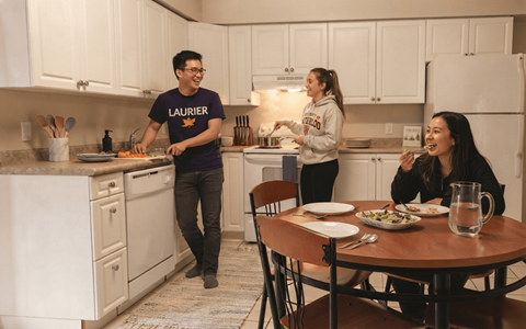 A man in a Laurier shirt is cooking in a kitchen with two women.