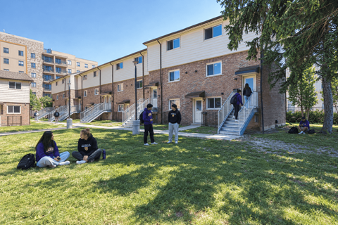 A group of people are sitting on the grass in front of a building.