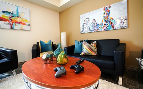 A living room with a black couch, a wooden table, and two gaming controllers on the table.