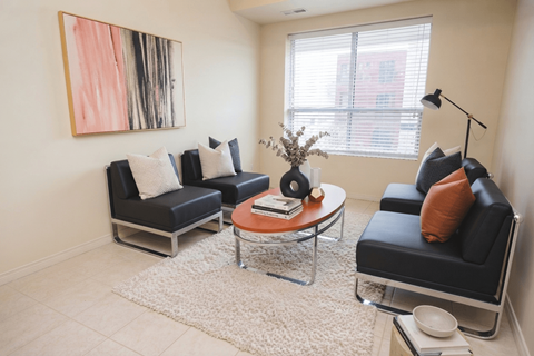 A living room with a black couch, a coffee table, and a painting on the wall.