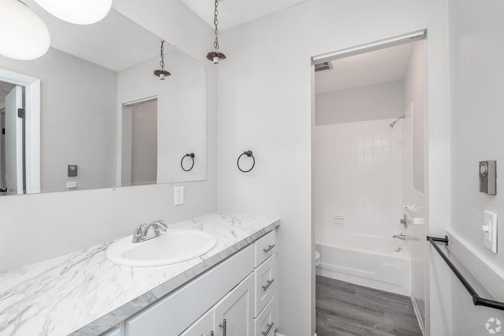 A white bathroom with a marble countertop and a walk-in shower.
