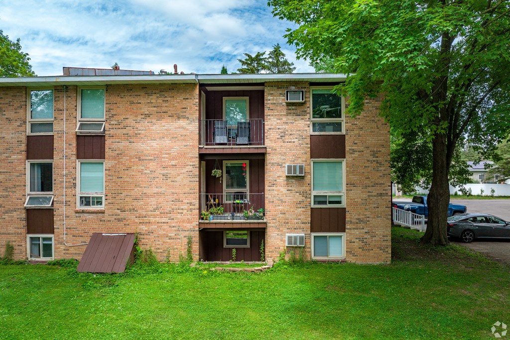 A brick building with a balcony and a tree in front.