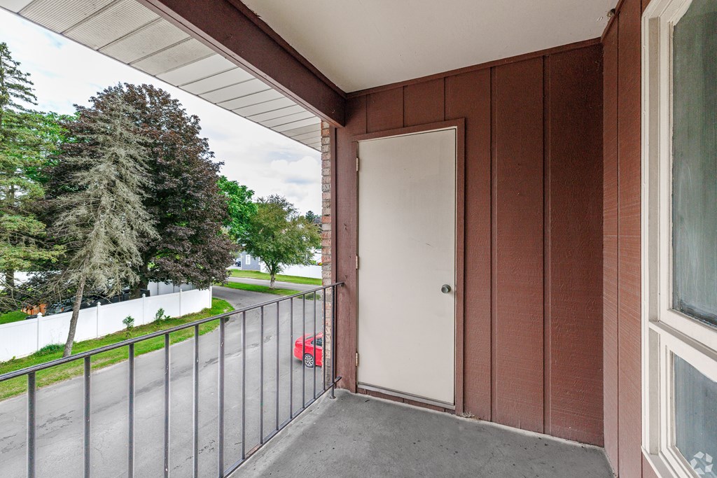 A red car is parked on the street behind a fence.