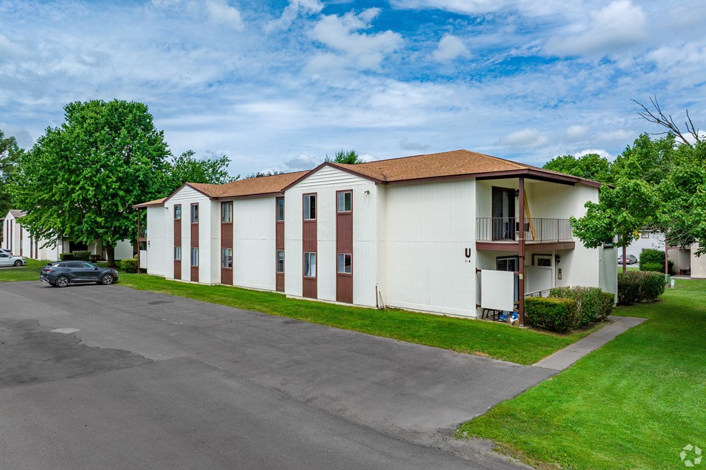 A white building with brown roof and a car parked in front.