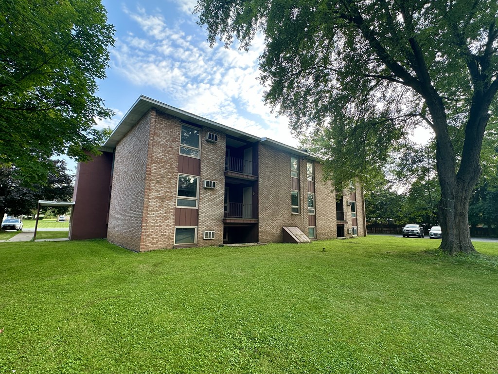 an apartment building with a green lawn and trees