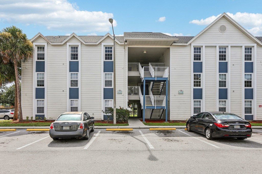 Two cars are parked in a parking lot in front of a white building with blue trim.
