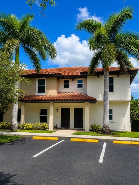 A two-story house with a red tile roof and a palm tree in front.