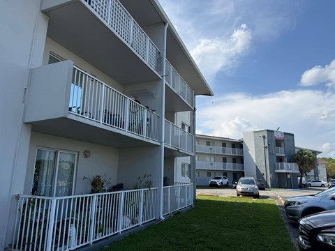 A white apartment building with balconies and cars parked in the background.