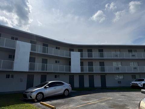 A silver car is parked in a parking lot in front of a white building.