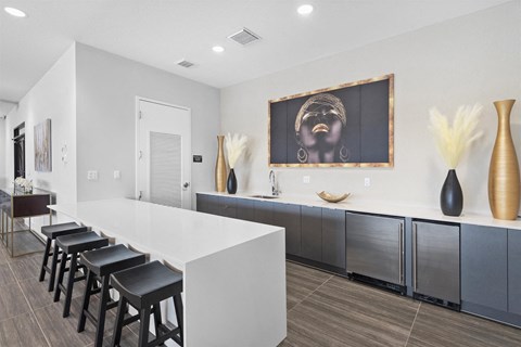 a kitchen with a long white counter and a row of black chairs