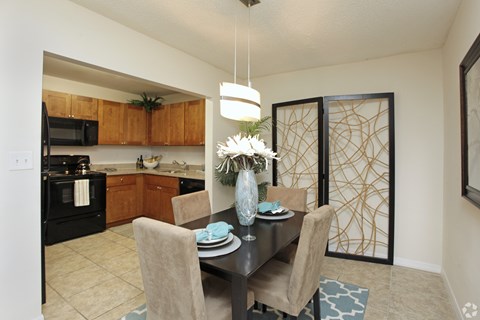 A dining room with a table set for two and a vase of flowers.