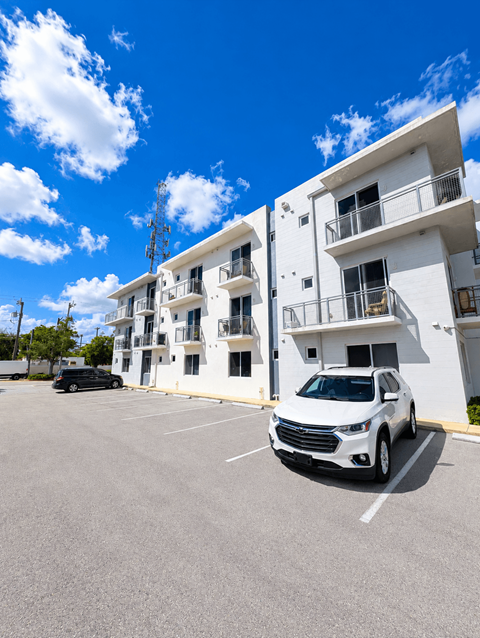 A white car is parked in a parking lot in front of a white building.