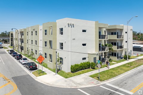 A street view of a residential area with apartment buildings and cars parked on the side of the road.