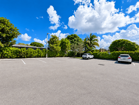 Two cars are parked in a parking lot with trees and a blue sky in the background.