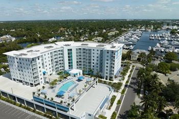 A large white hotel with a pool in the middle of a parking lot.