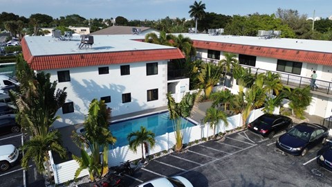 A white building with a red roof is surrounded by a parking lot.