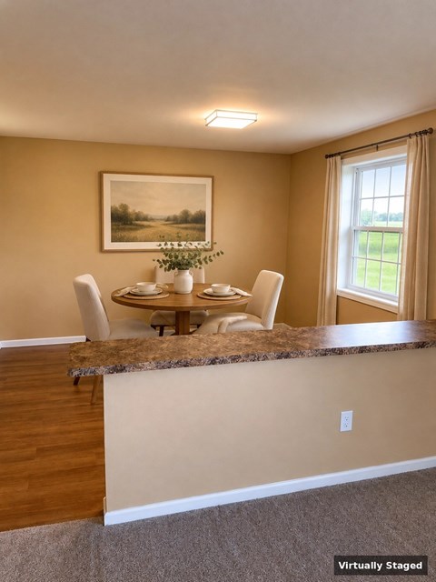 A dining room with a table set for four and a painting on the wall.