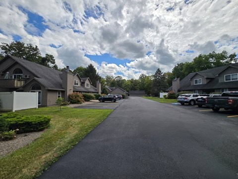 A residential street with houses on both sides and cars parked on the right side.
