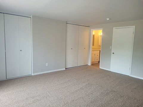 A room with white walls and carpeted floor with a door on the right.