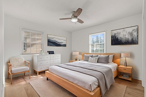 A bedroom with a bed, nightstand, chair, and two pictures on the wall.