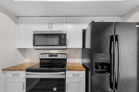 A black refrigerator stands in a kitchen with a stove and microwave above it.