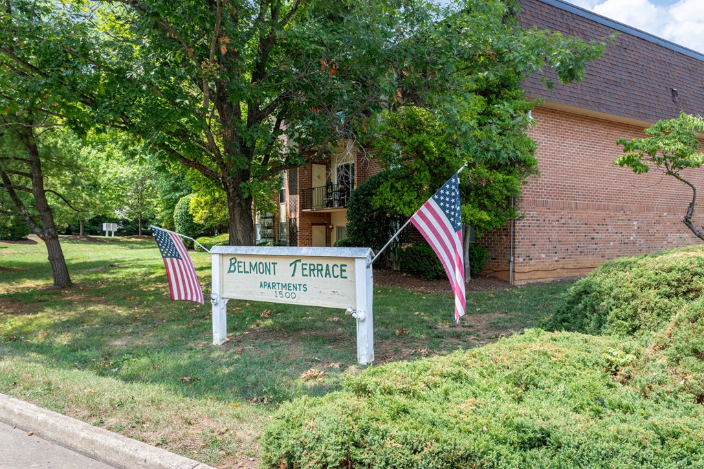 A sign for Belmont Terrace Apartments stands in front of a building with two American flags on either side.