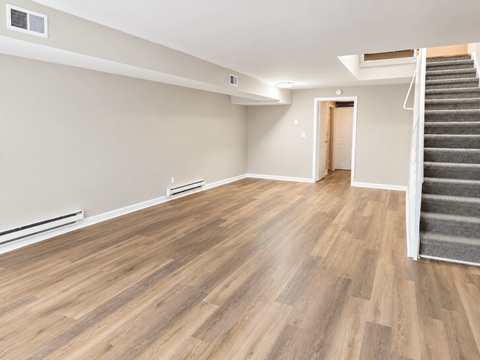A room with wooden flooring and a staircase leading to another room.